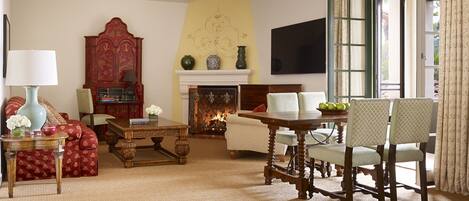 A traditional living room with a fireplace, a red cabinet, and a dining area with chairs and a table.