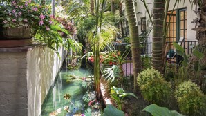 Un exuberante jardín interior con fuente de agua, plantas tropicales grandes y un área de descanso con vistas al jardín.