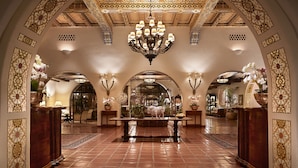 Un lobby imponente con una gran araña, arcos ornamentales y una mesa central con una figura decorativa de animal.