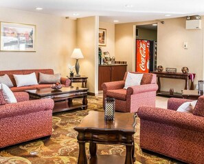 A hotel room with a patterned red sofa set, a wooden coffee table, a lamp, a Coca-Cola refrigerator, and a framed picture on the wall. - Quality Inn Holland - Toledo (Holland)