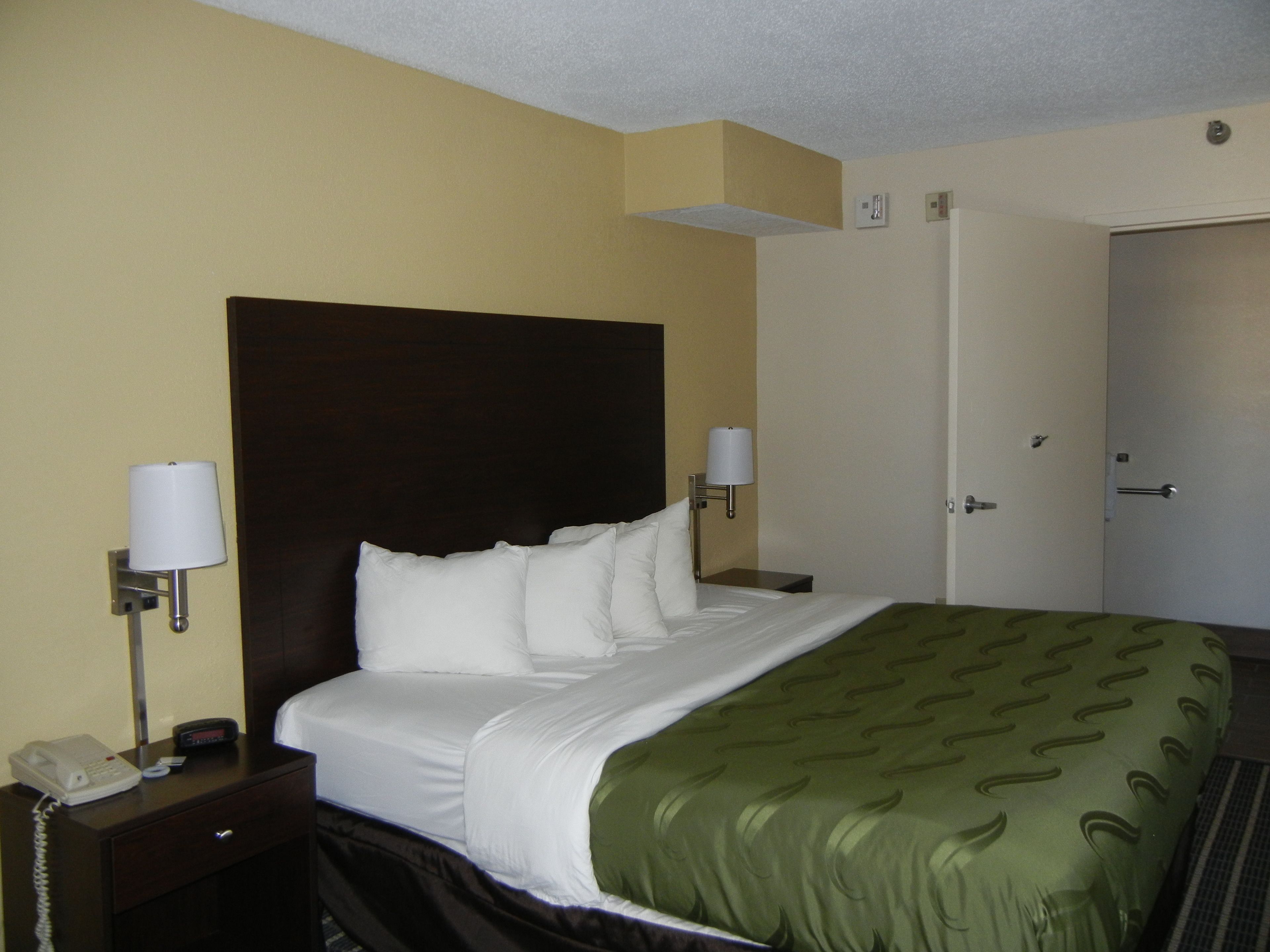 A hotel room with a large bed, two bedside lamps, a telephone, and a door.