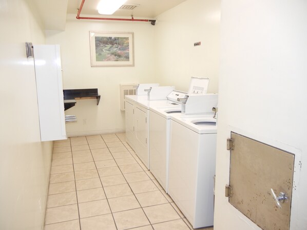 A laundry room with a white sink, two washing machines, and a drying machine.