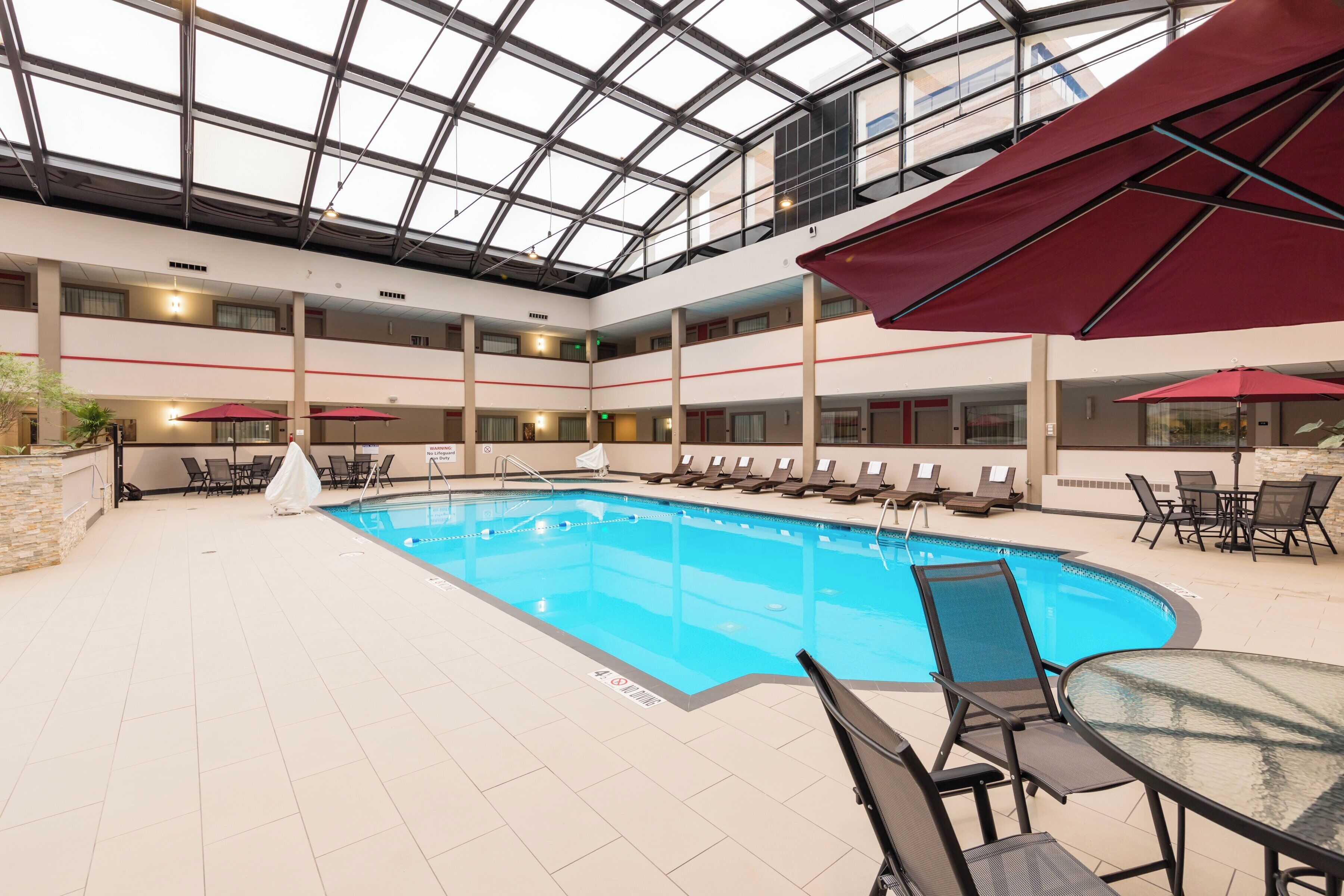 Une piscine intérieure à plusieurs niveaux, dotée de chaises longues et de parasols, entourée d’un sol carrelé et surmontée d’un plafond en verre.
