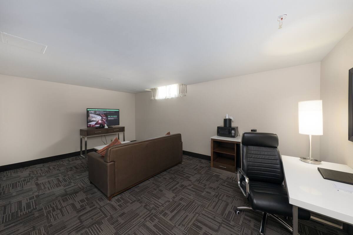 A hotel room with a sofa, a desk, a chair, a television, and a lamp.