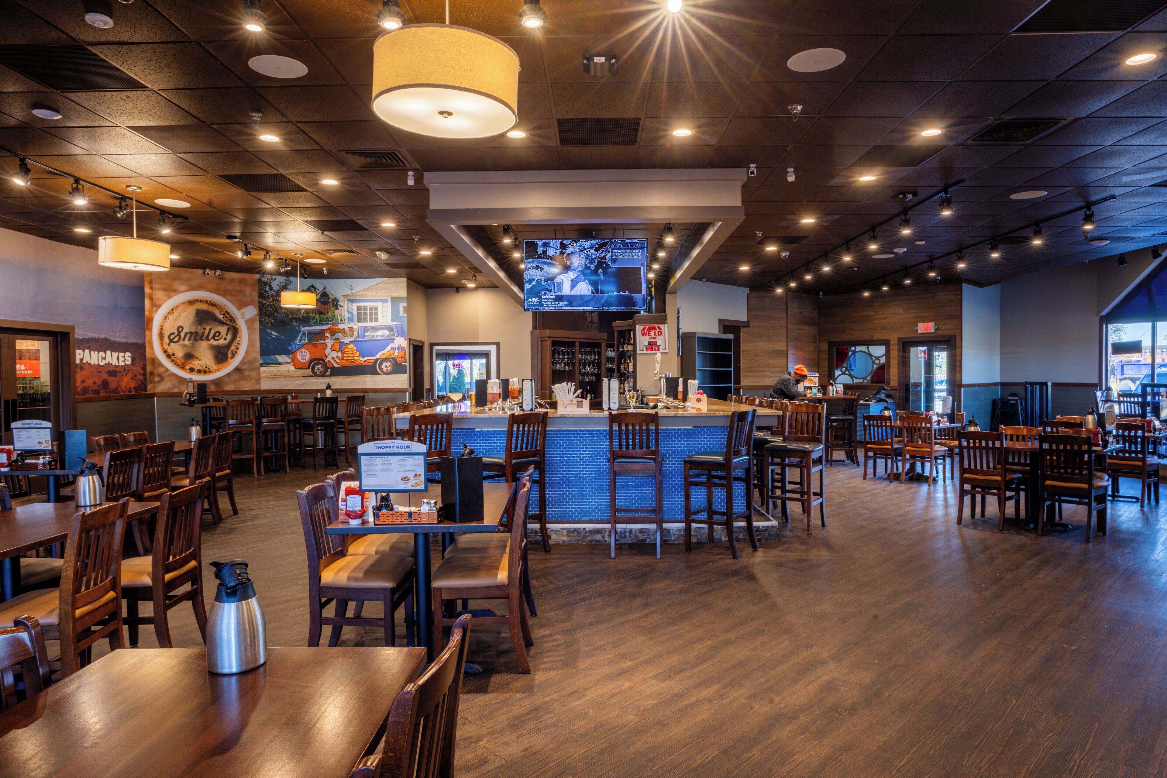 A restaurant with wooden tables and chairs, a bar area, and a television screen.