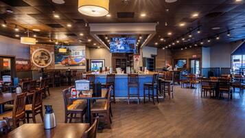 A restaurant with wooden tables and chairs, a bar area, and a television screen.