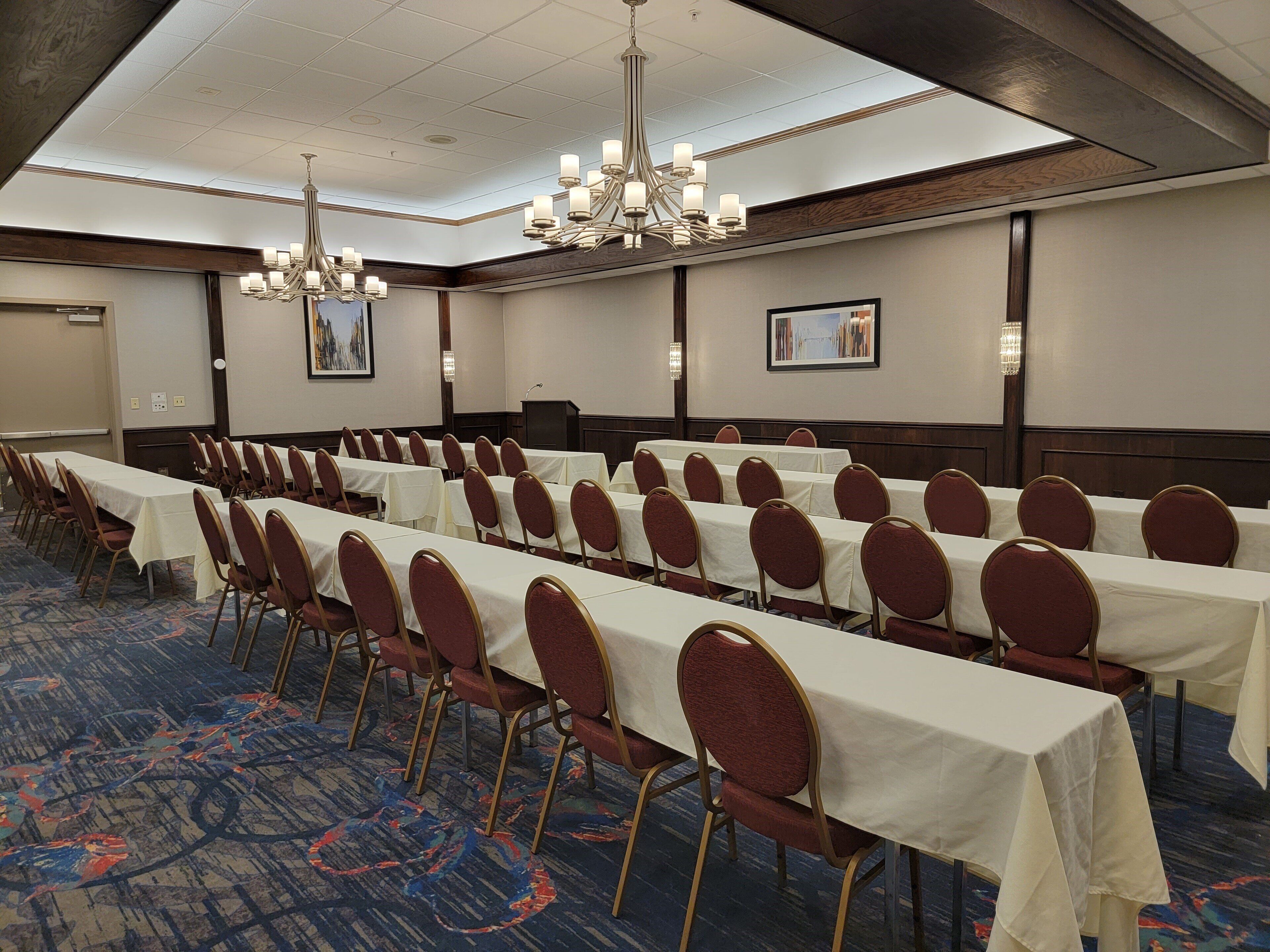 A conference room with rows of tables and chairs, a chandelier, and a projector screen.