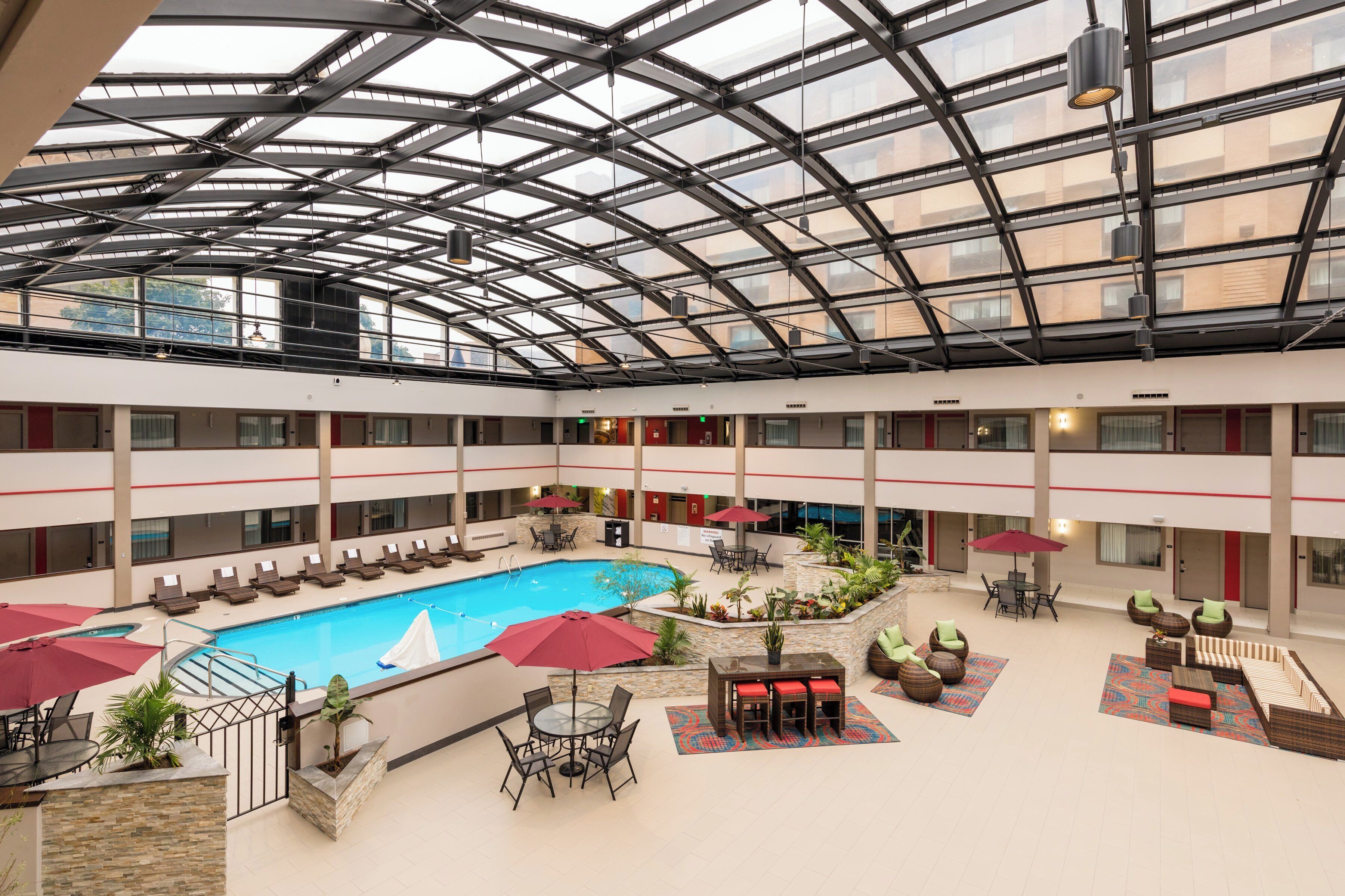 A multi-level indoor pool area with a glass ceiling, lounge chairs, and a central pool.