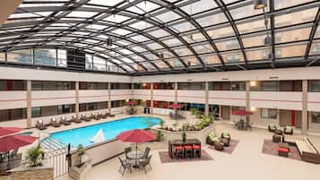 A multi-level indoor pool area with a glass ceiling, lounge chairs, and a central pool.