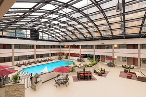A multi-level indoor pool area with a glass ceiling, lounge chairs, and a central pool. - Holiday Inn Brookfield - ​​Milwaukee by IHG (Brookfield)