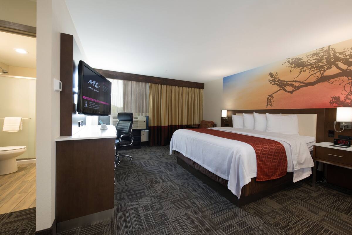 A hotel room with a bed, a desk, a chair, a TV, and a painting on the wall.