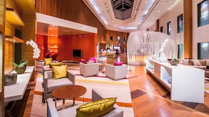 Un hall d'hotel modern amb una zona d'estar central, una recepció i un disseny de sostre distintiu.