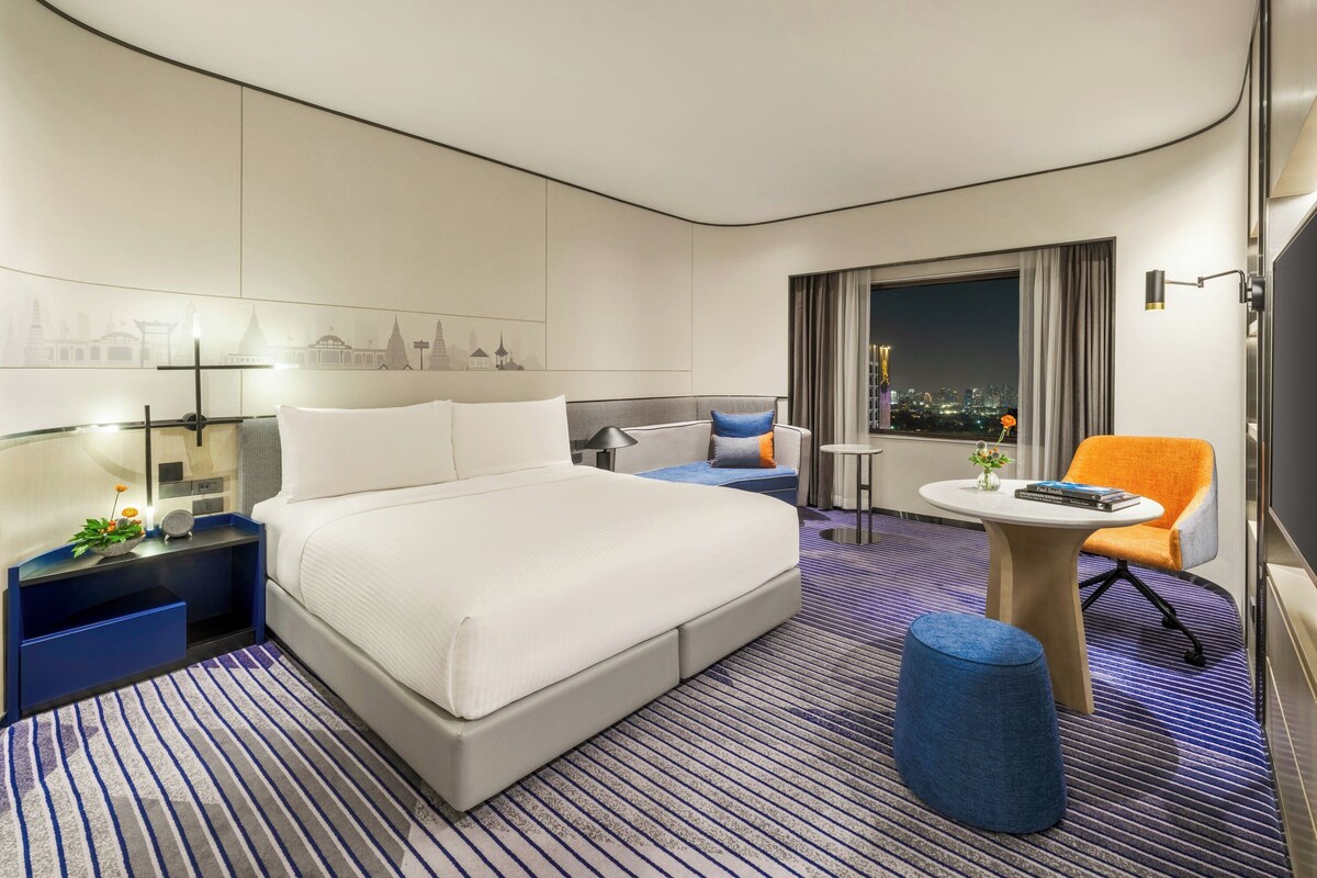 Una habitación de hotel moderna con una cama grande, un sofá, una mesita y una silla.
