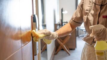 A person cleaning a door handle with a yellow cloth and a spray bottle labeled "DO NOT DRINK".