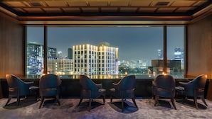 A modern hotel room with a large window offering a city view, a carpeted floor, and a seating area with chairs. - Crowne Plaza Bangkok Lumpini Park by IHG (Bangkok)