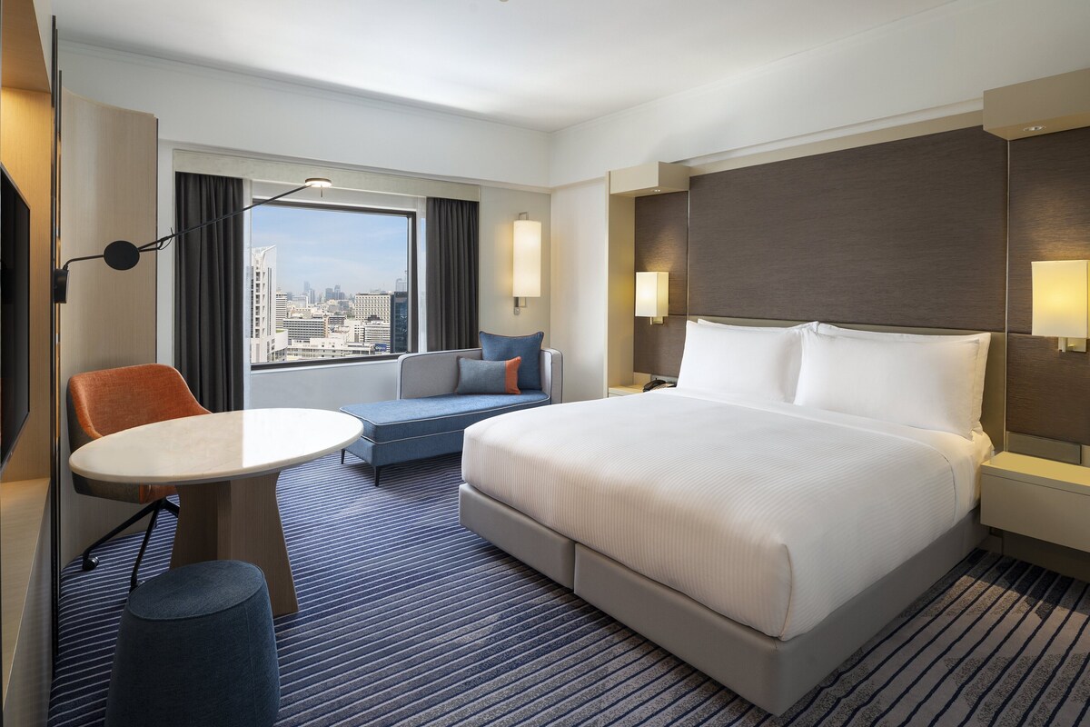 Habitación de hotel con una cama grande, un escritorio, una silla y vistas a la ciudad.
