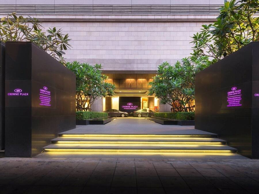 Entrada de hotel con diseño moderno, que presenta una escalera central que conduce a la recepción, rodeada de vegetación e iluminada con luz ambiental.