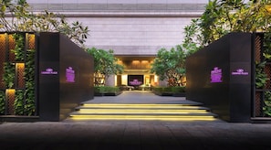 Entrada d'hotel amb un disseny modern, que destaca una escala central cap a l'entrada, envoltada de vegetació i il·luminada amb una llum ambiental.