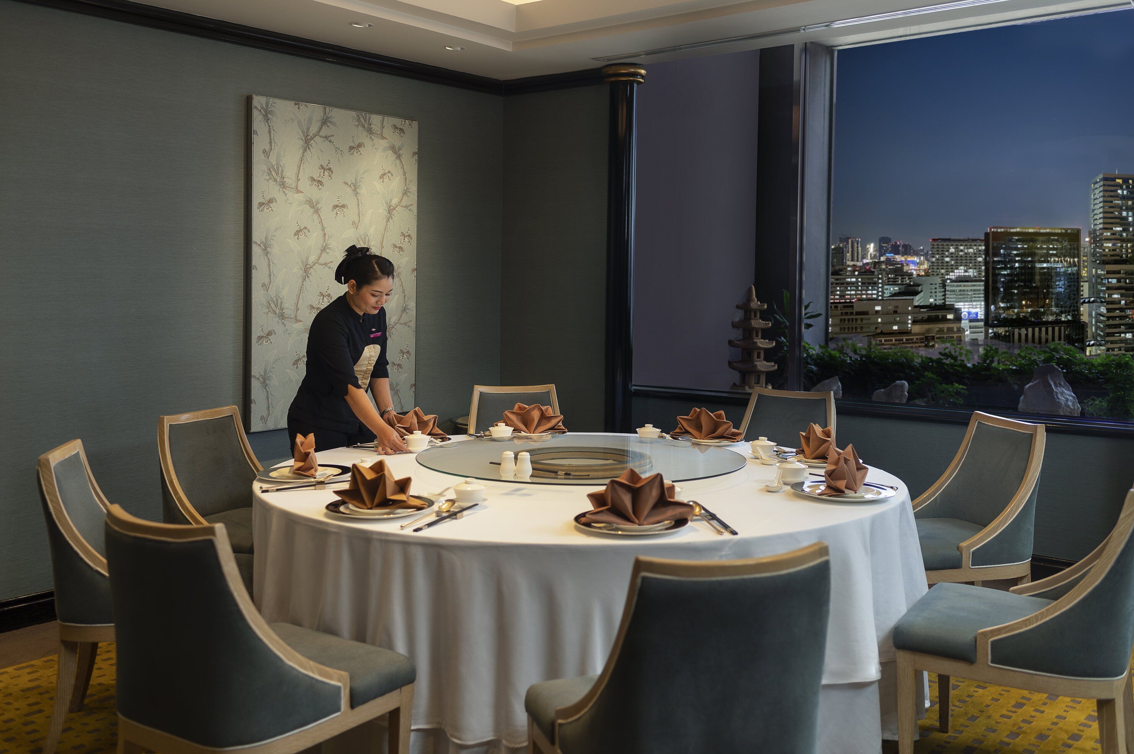 Comedor con una mesa redonda dispuesta para seis personas, vistas de la ciudad a través de amplios ventanales y un cuadro abstracto grande en la pared.