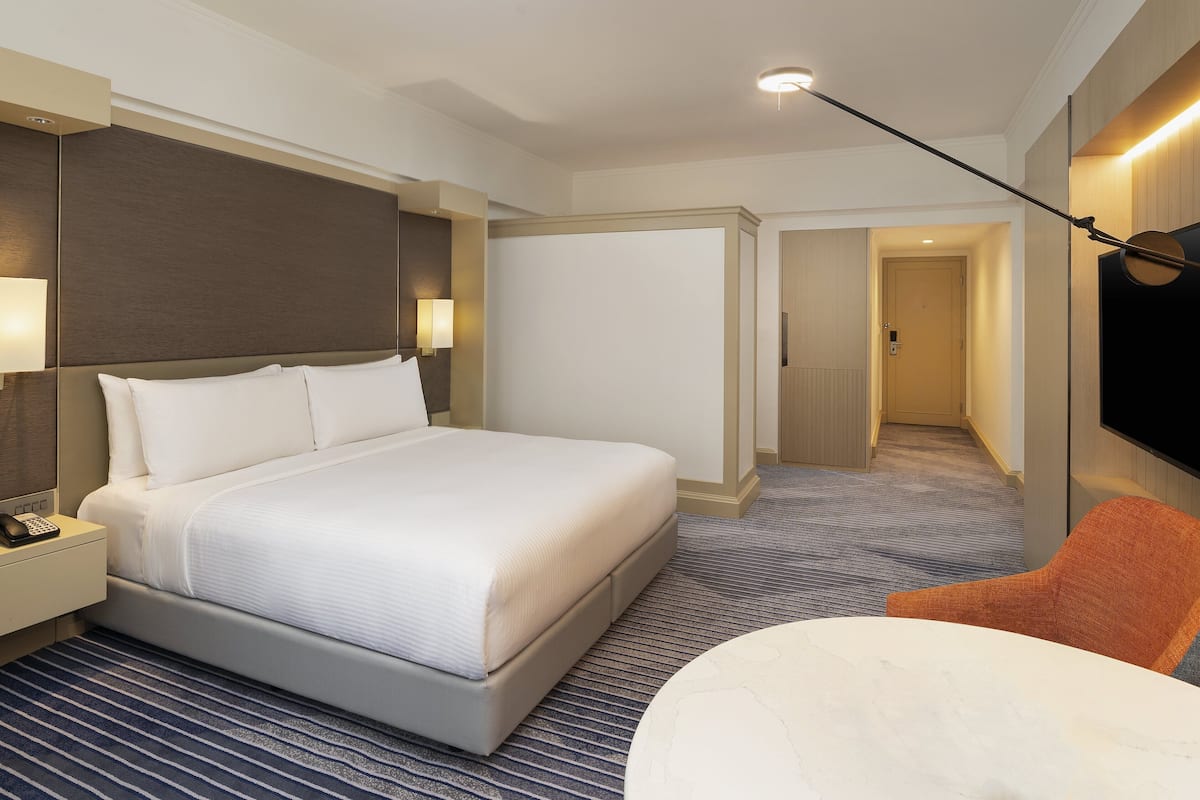 Habitación de hotel con una cama grande, un escritorio con teléfono, un televisor de pantalla plana en la pared y una silla.
