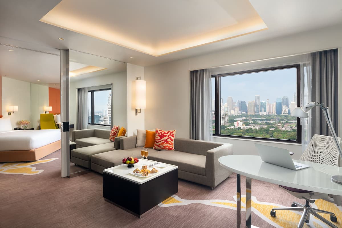 Una habitación de hotel moderna con cama, sofá, mesa de comedor y una computadora portátil sobre un escritorio.