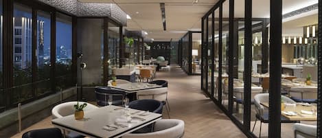 Un comedor moderno con mesas, sillas, ventanas amplias y vistas a la ciudad.