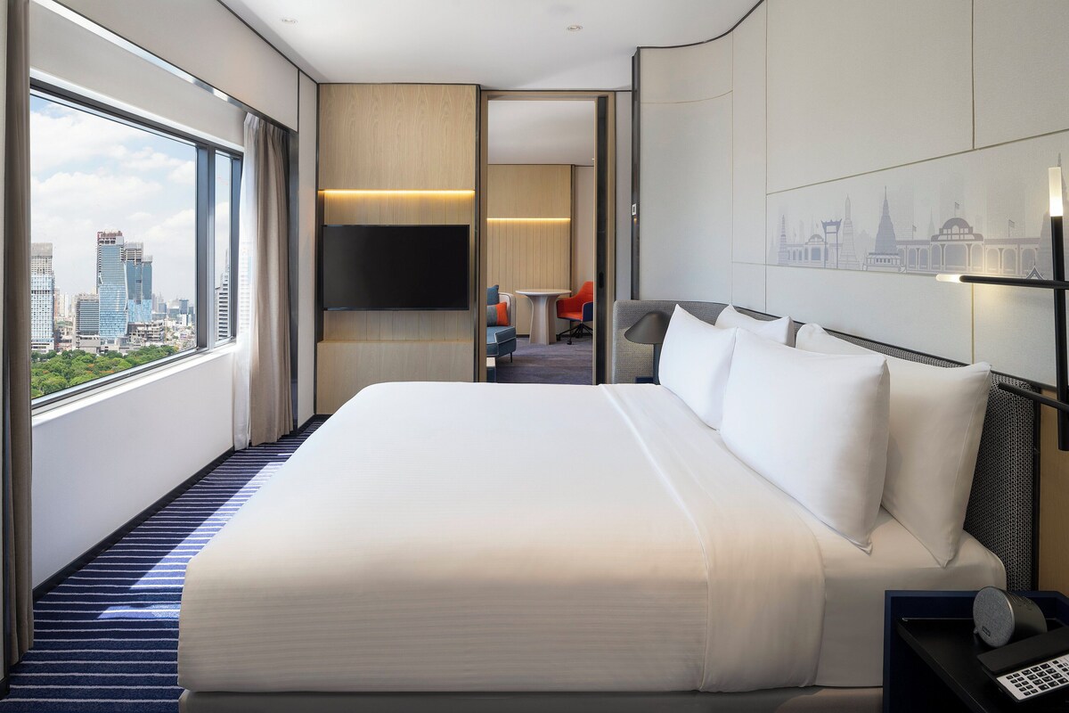 Habitación de hotel con una cama grande, televisión y vista a la ciudad.