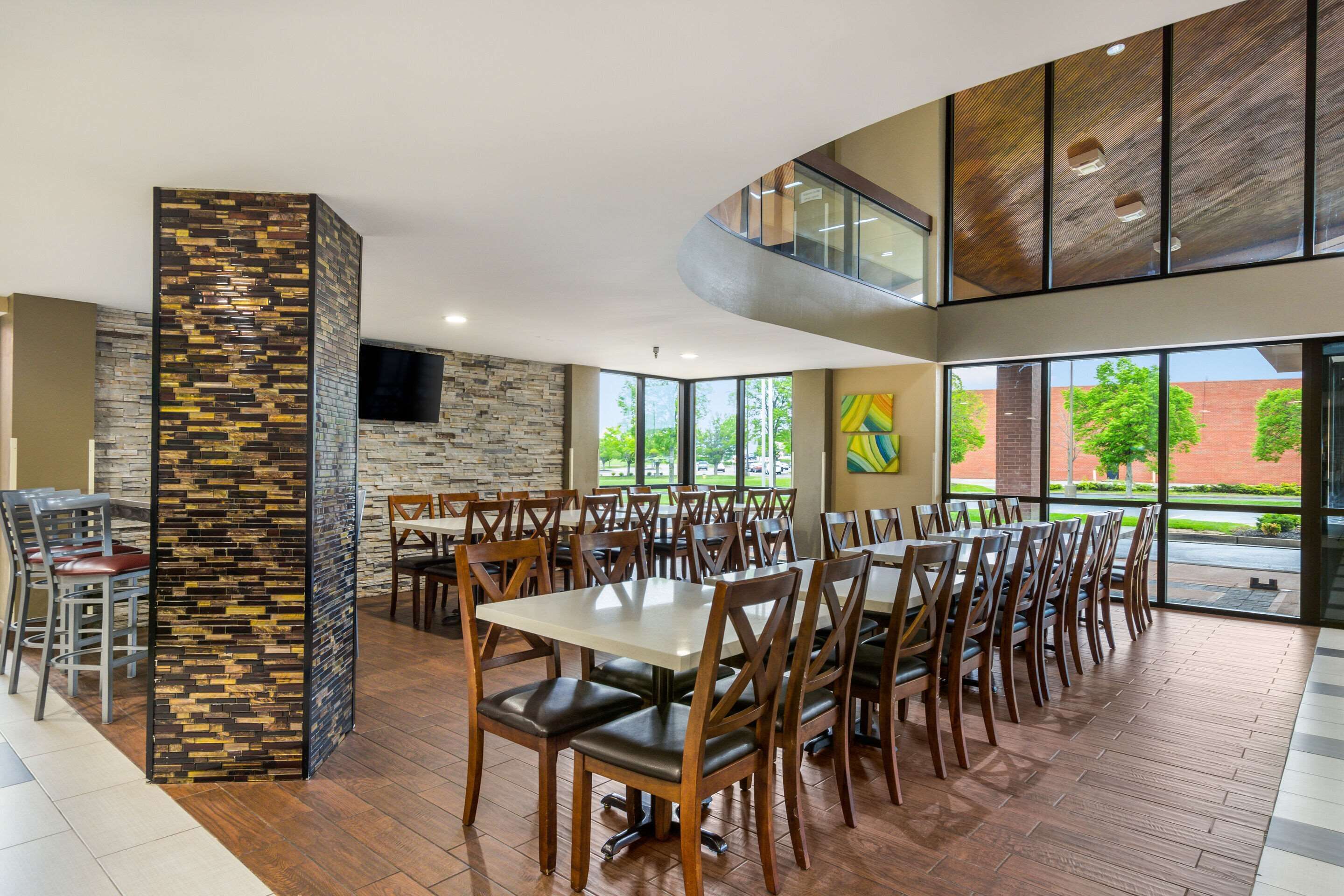 A spacious dining area with multiple tables and chairs, a stone accent wall, and large windows offering a view of the outdoors.