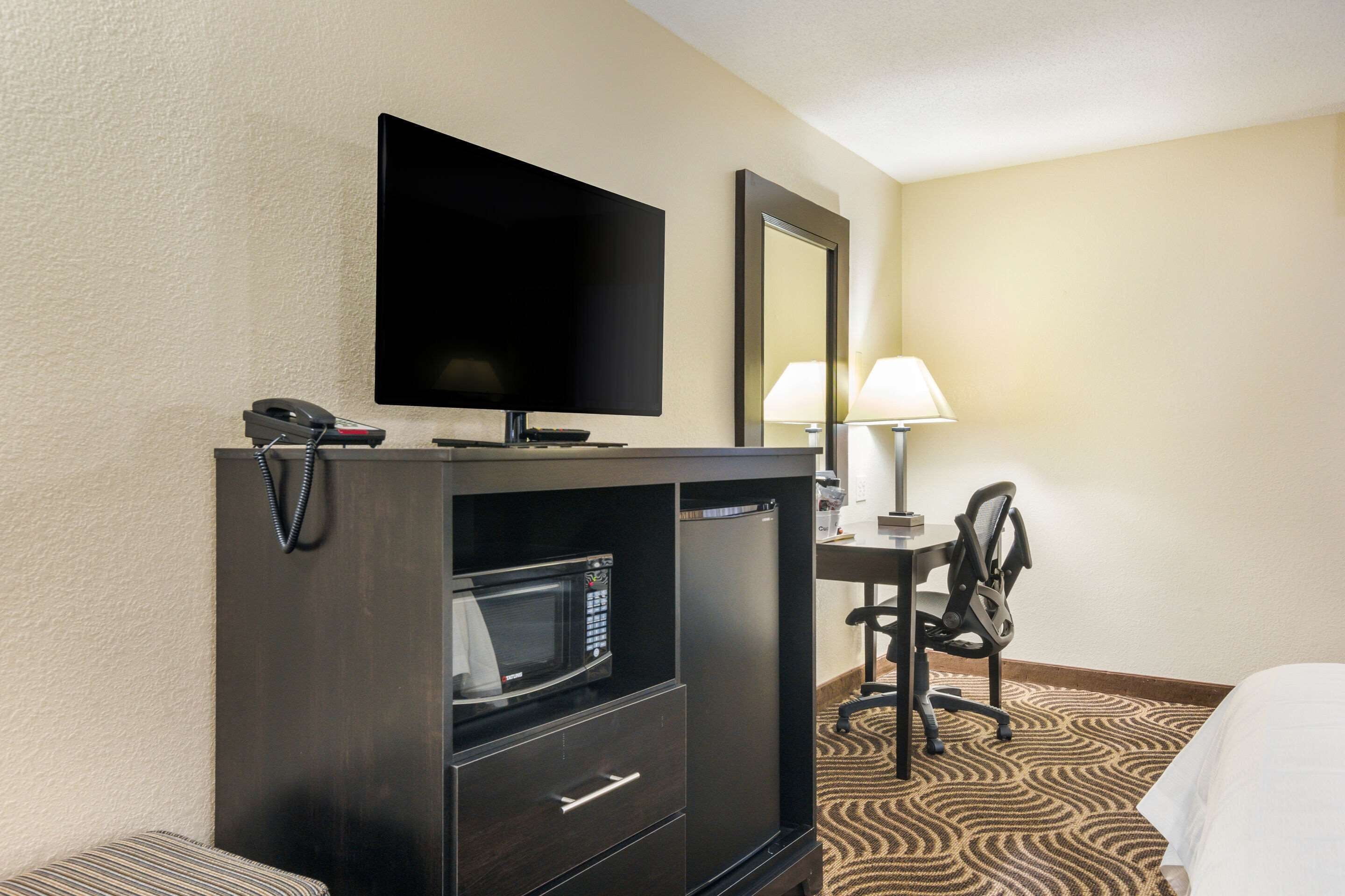 A hotel room with a flat-screen TV, a microwave, a desk with a chair, and a bed.