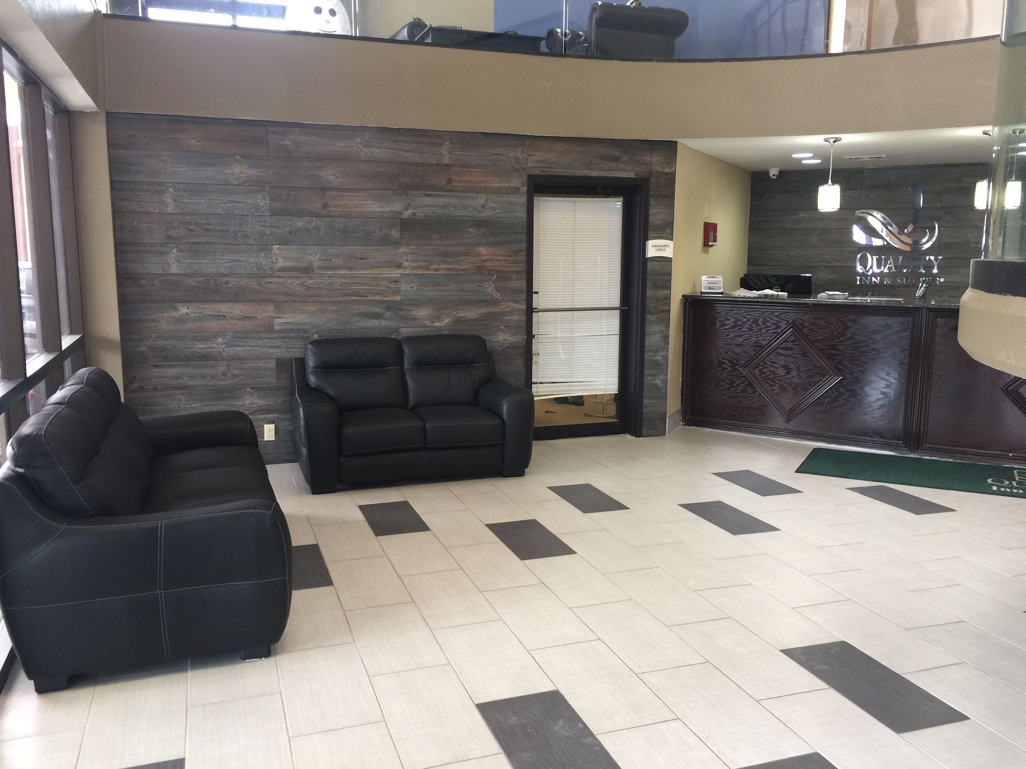 A lobby with a reception desk, two black leather sofas, a wooden wall, and a tiled floor.