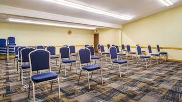 Un salón de conferencias con filas de sillas azules y una alfombra estampada.
