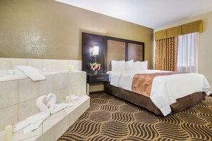 A hotel room with a large bed, a separate bathroom with a bathtub, and a patterned carpet.
