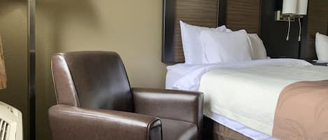A hotel room with a bed, a brown leather chair, a lamp, and a wall-mounted light fixture.
