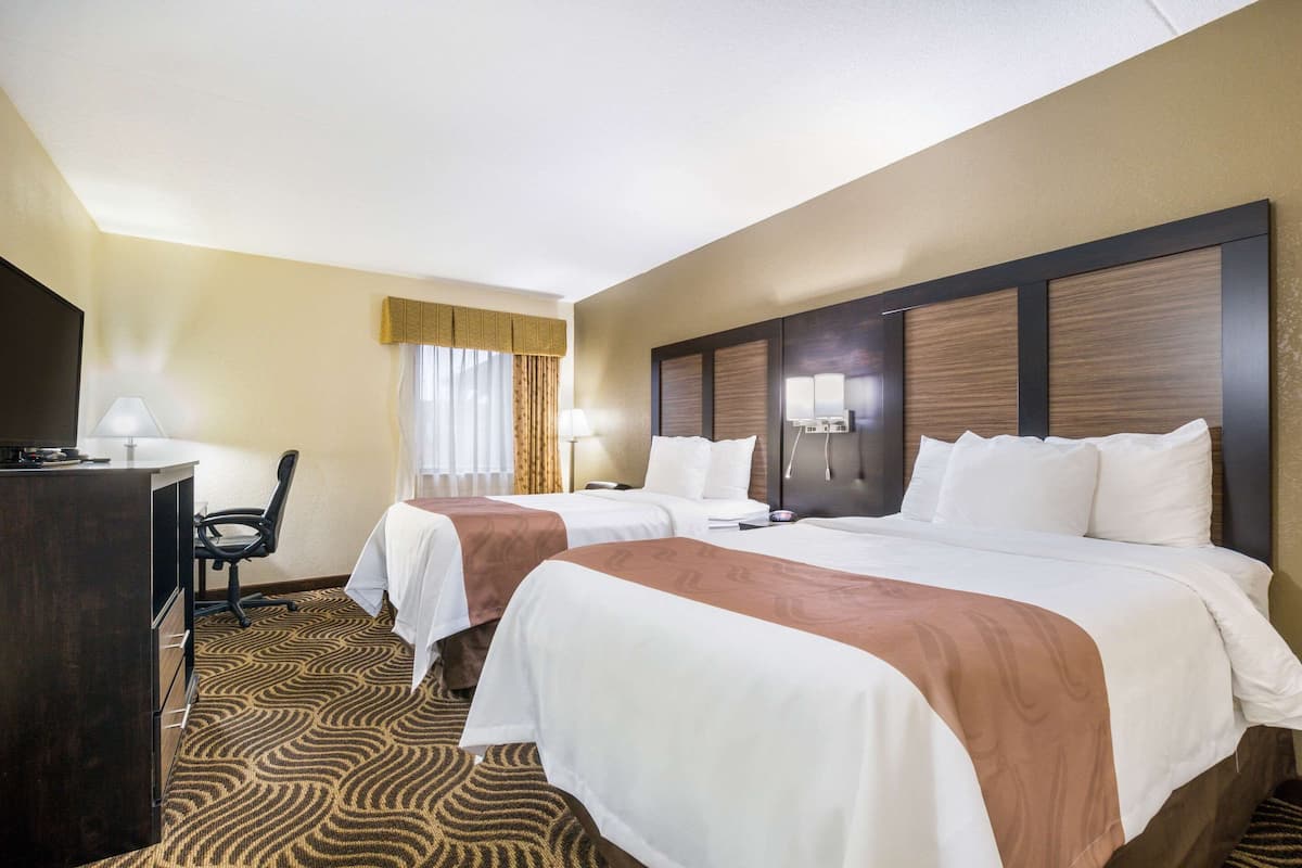 A hotel room with two beds, a desk, and a chair.