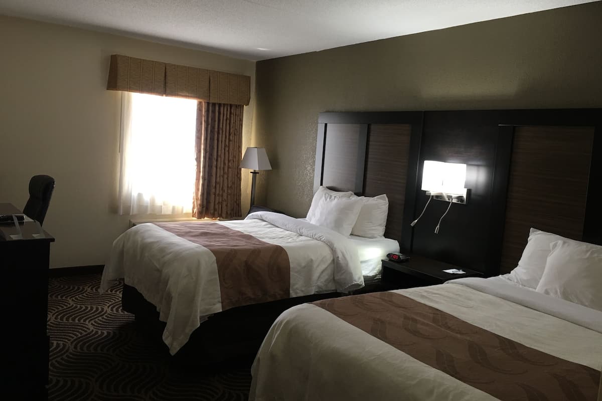 A hotel room with two beds, a desk, a lamp, and a window with curtains.
