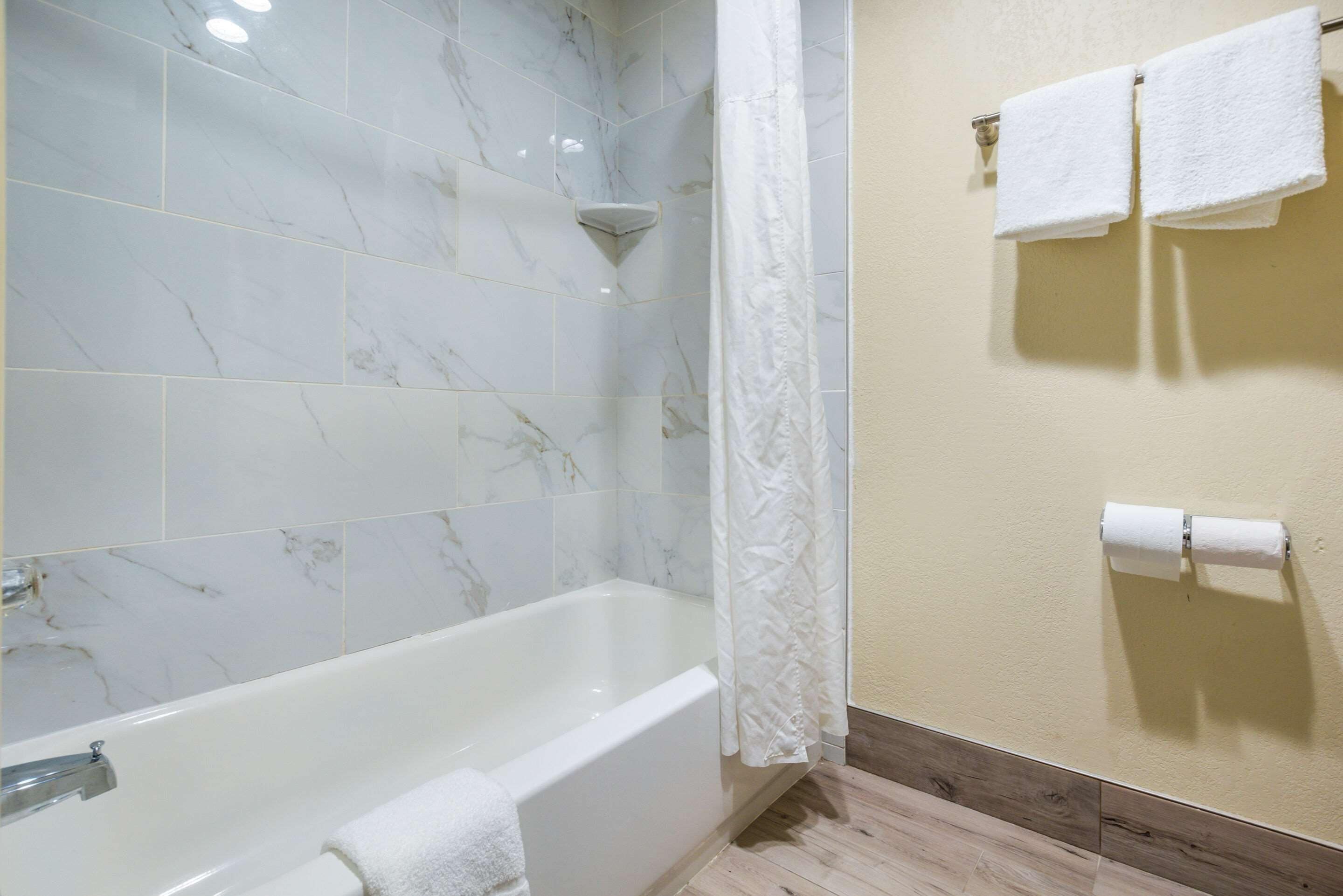 A bathroom with a bathtub, a shower curtain, and two towels hanging on the wall.
