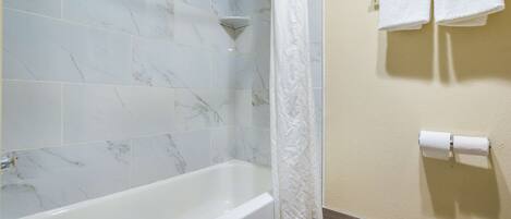A bathroom with a bathtub, a shower curtain, and two towels hanging on the wall.