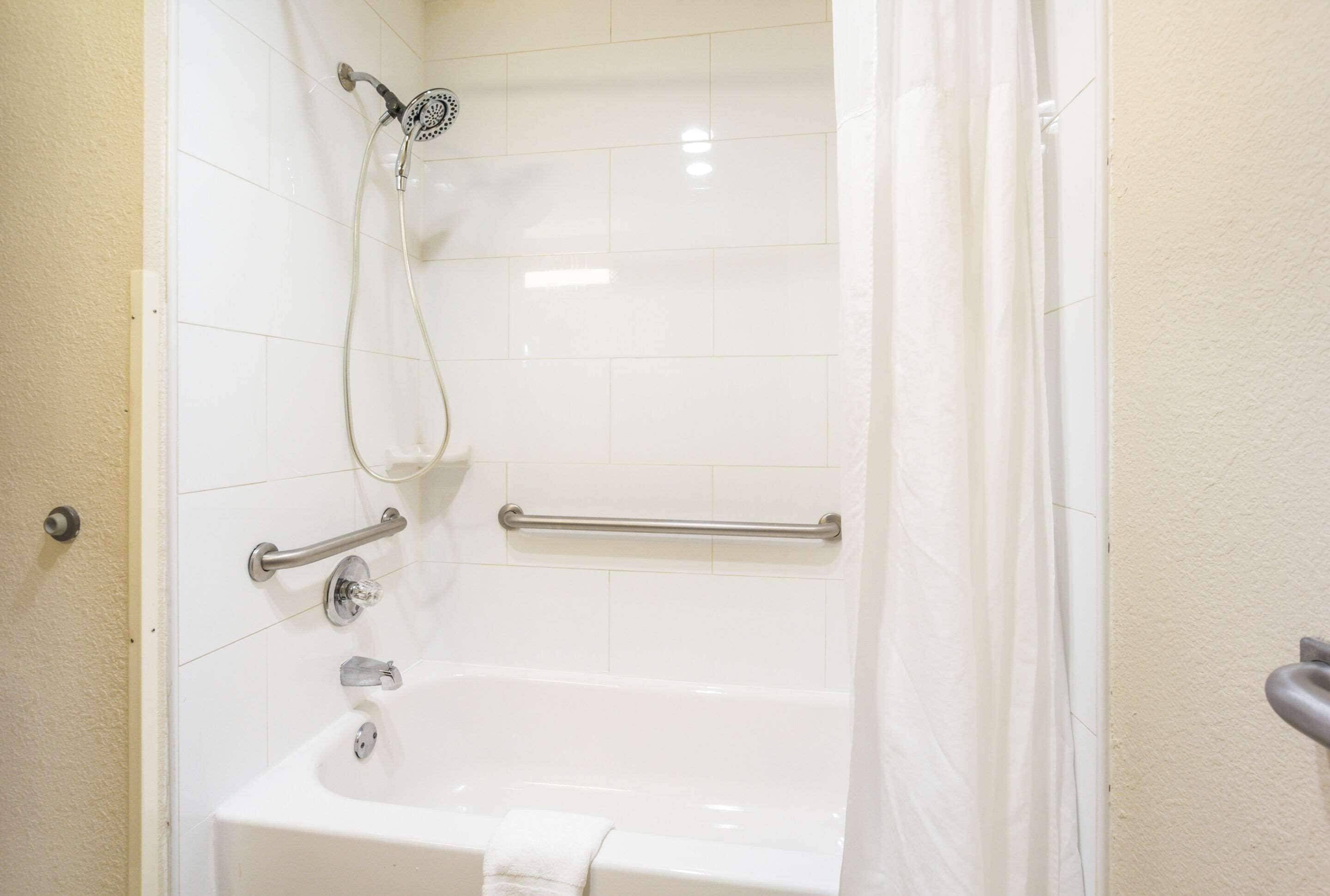 A bathroom with a bathtub, a showerhead, and grab bars.