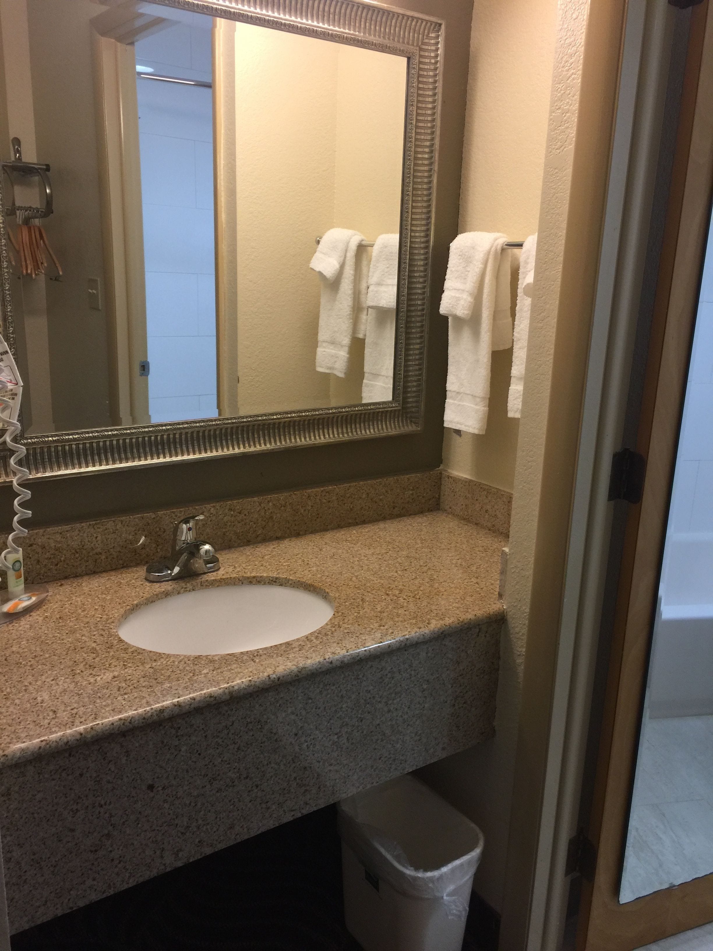 A bathroom with a granite countertop, a white sink, a mirror, and a towel rack with white towels.