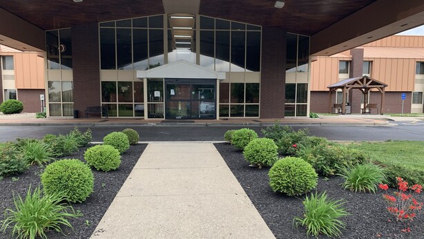 A building entrance with a covered walkway, surrounded by landscaped gardens and a parking area. - Quality Inn & Suites Florence - Cincinnati South (Florence)