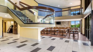 A spacious lobby with a curved staircase, a seating area with chairs, and large windows offering a view of the outdoors. - Quality Inn & Suites Florence - Cincinnati South (Florence)