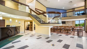 A hotel lobby with a staircase, a reception desk, and a dining area with tables and chairs. - Quality Inn & Suites Florence - Cincinnati South (Florence)