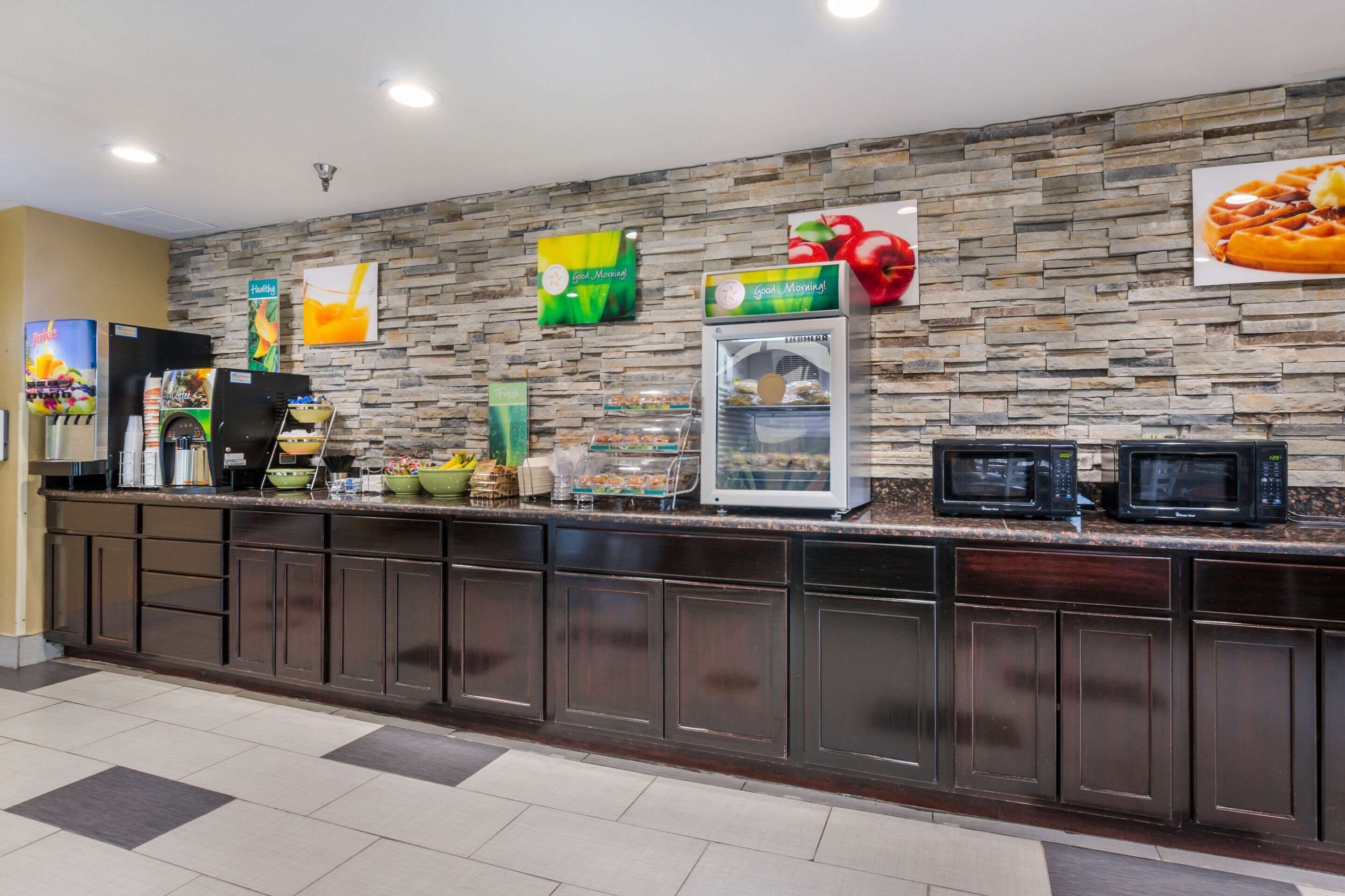 A breakfast bar with a stone wall backdrop, a refrigerator, and a microwave.