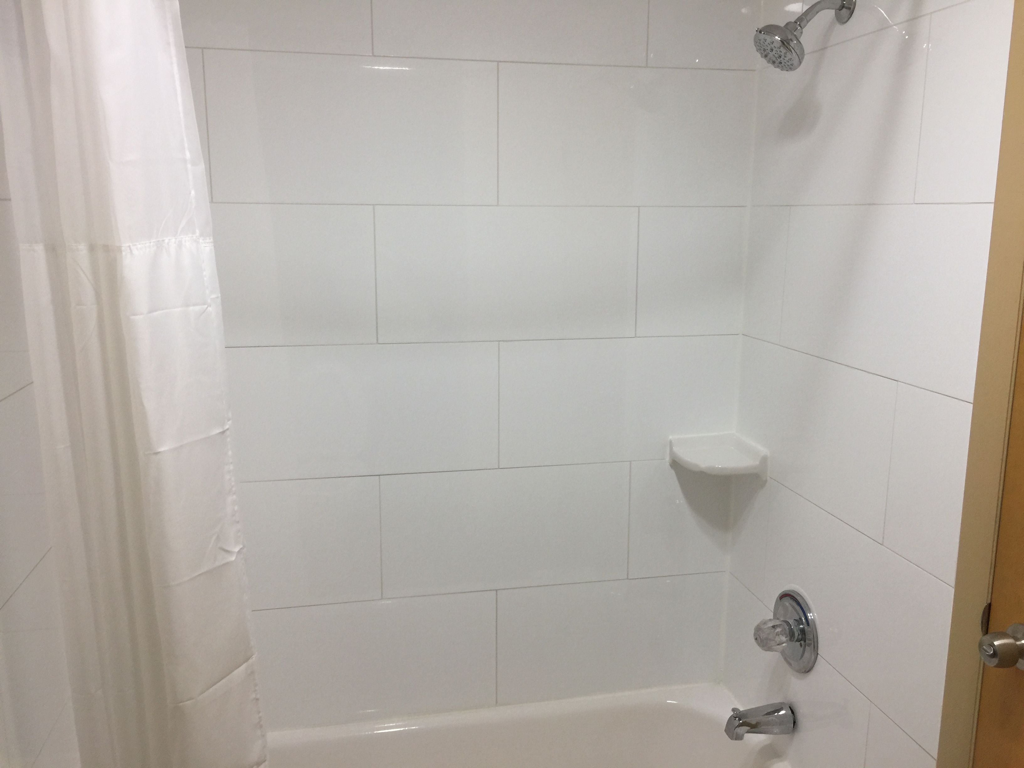 A bathroom with white tiled walls, a shower, and a toilet.