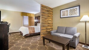 A hotel room with a bed, a sofa, a coffee table, a desk with a lamp, and a framed picture on the wall. - Quality Inn & Suites Florence - Cincinnati South (Florence)