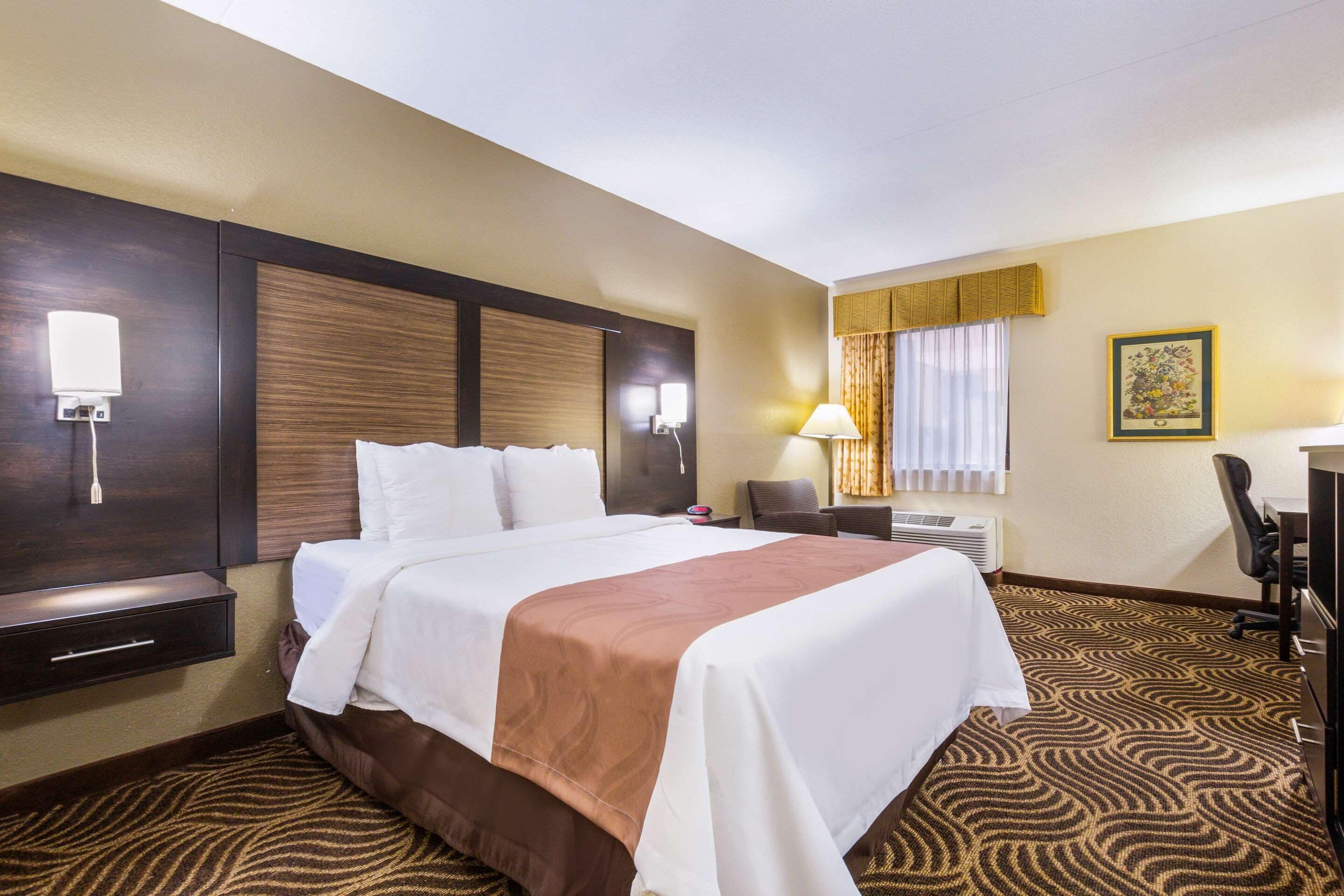 Una habitación de hotel con cama, mesita de noche, lámpara y escritorio con silla.
