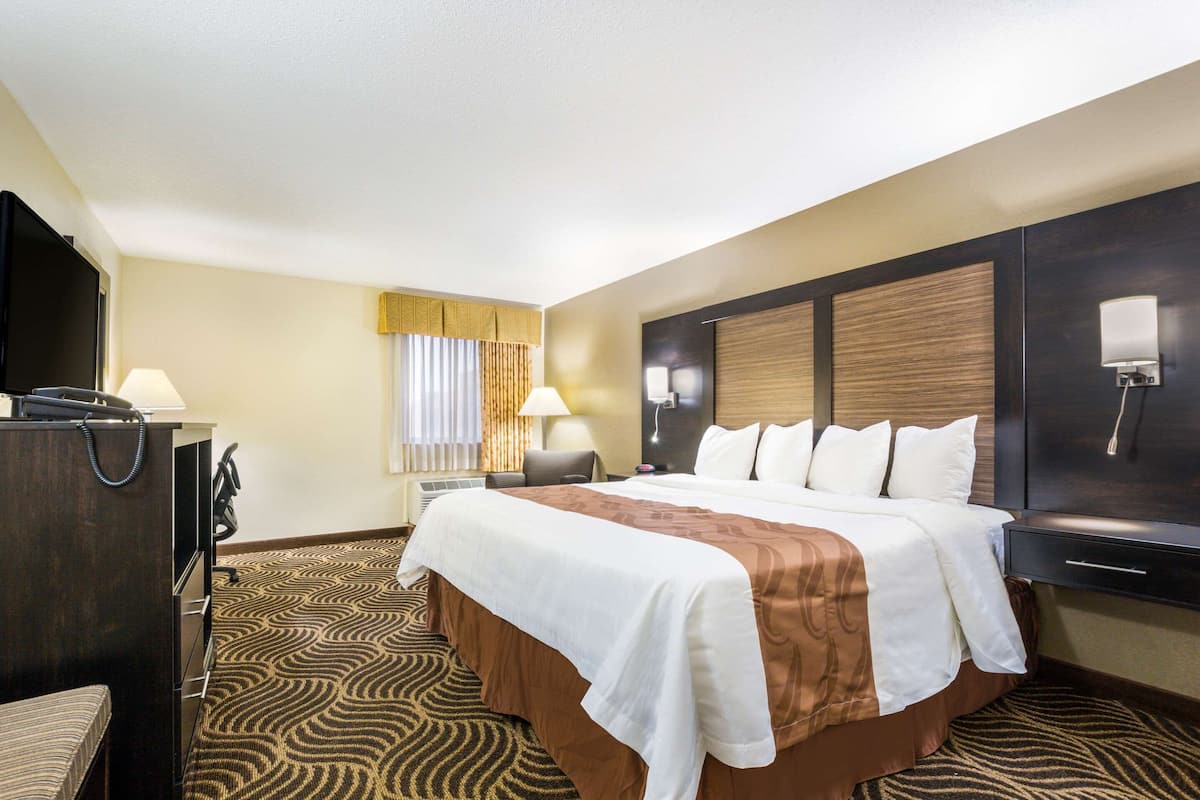 A hotel room with a large bed, a desk with a computer, a chair, a lamp, and a television.
