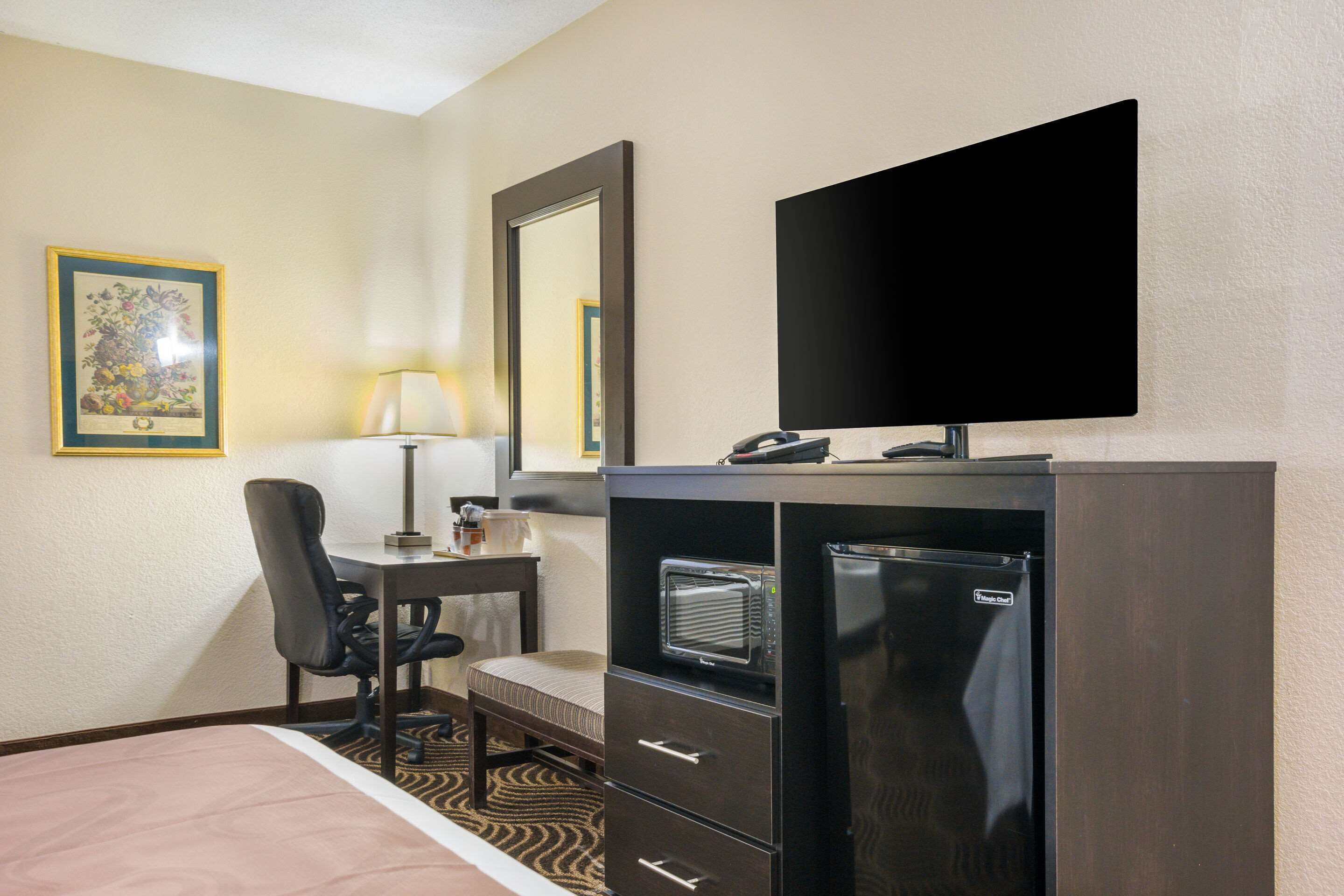 A hotel room with a bed, a desk with a chair, a flat-screen TV, a minibar, and a refrigerator.