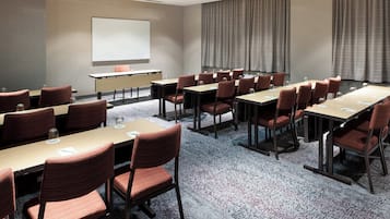 Un salón de conferencias con varias mesas y sillas, una pizarra y una pantalla para proyector.