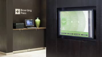 Un panel informativo digital en el vestíbulo de un hotel, con un letrero que dice 'Boarding Pass' y una computadora portátil sobre una estantería.